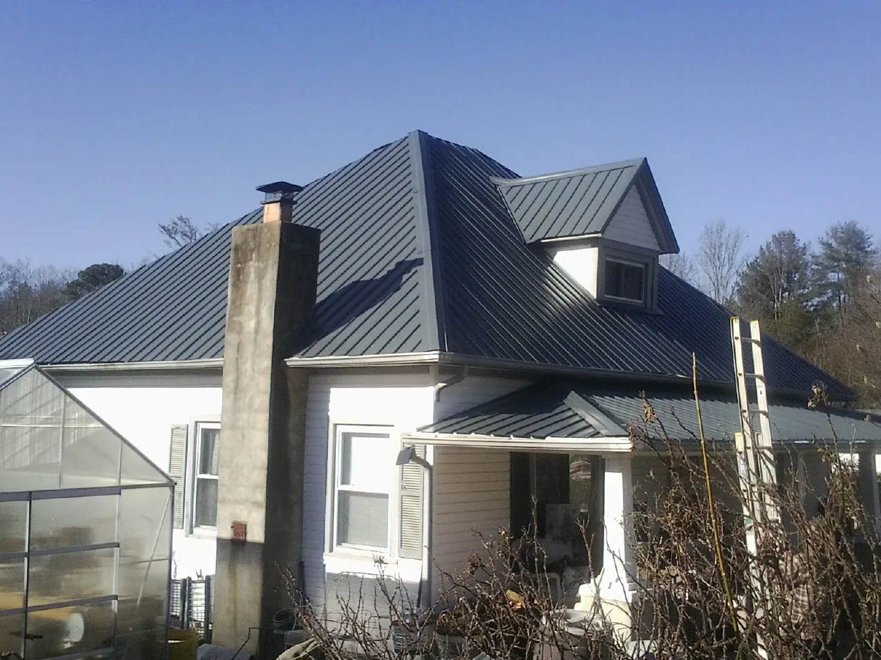 Dark blue standing seam metal roof on a white farmhouse with dormer — Slate & Tile Roof Repair by Roofing Brothers in Wellesley