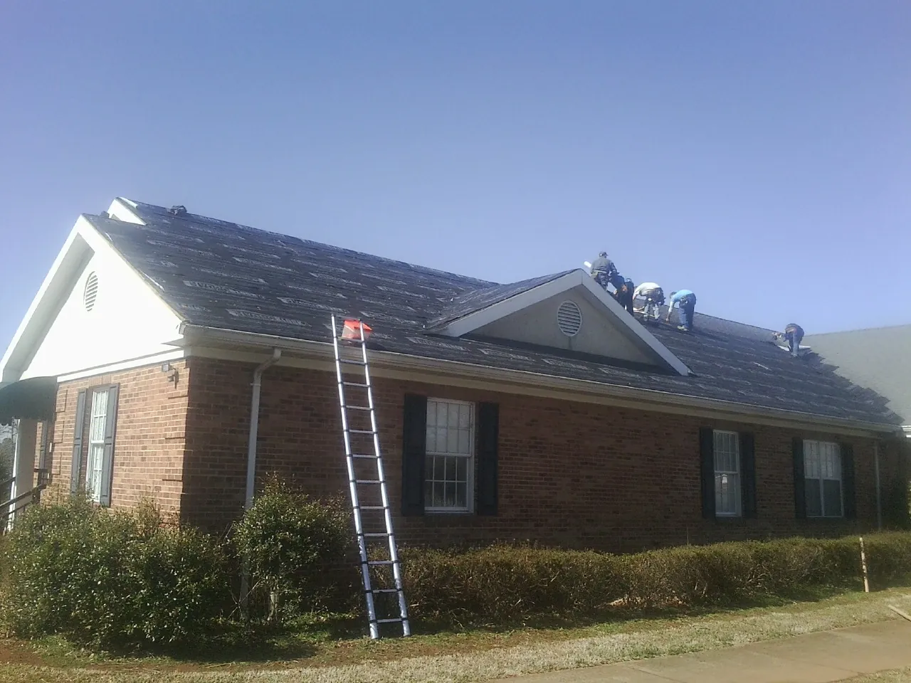 Crew tearing shingles off a brick ranch roof with a ladder set — Emergency Roof Repair work by our crew in Wellesley