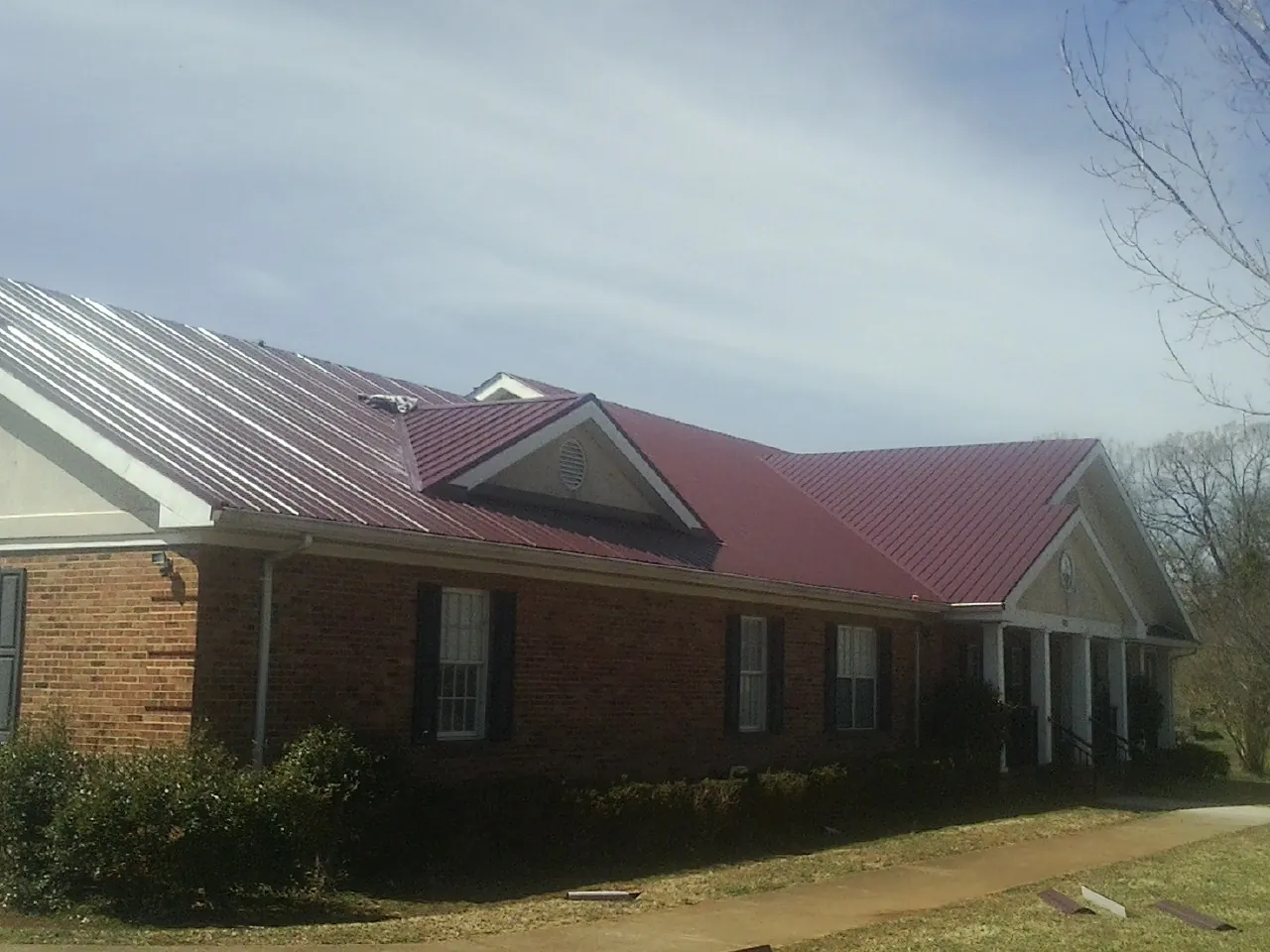 Red metal roof with gabled entries on a long brick building, from a Hail Damage Roof Repair job in Wellesley