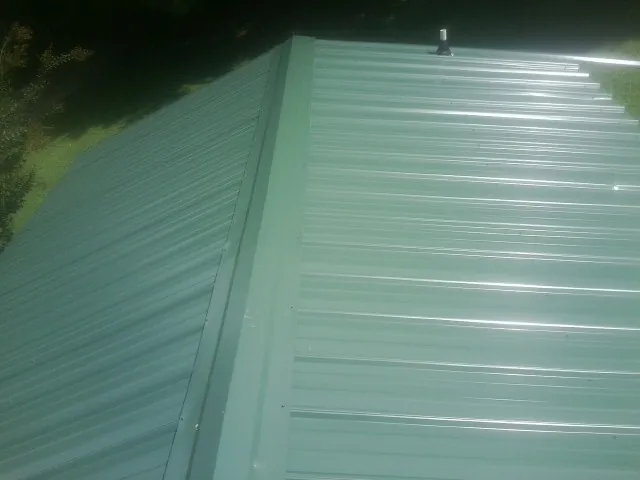 New green metal panels meeting at the ridge of a roof — Flat Roof Repair work by our crew in Wellesley