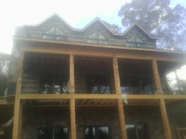 Dormers and porch framing on a large log home under construction — Roof Coating work by our crew in Wellesley